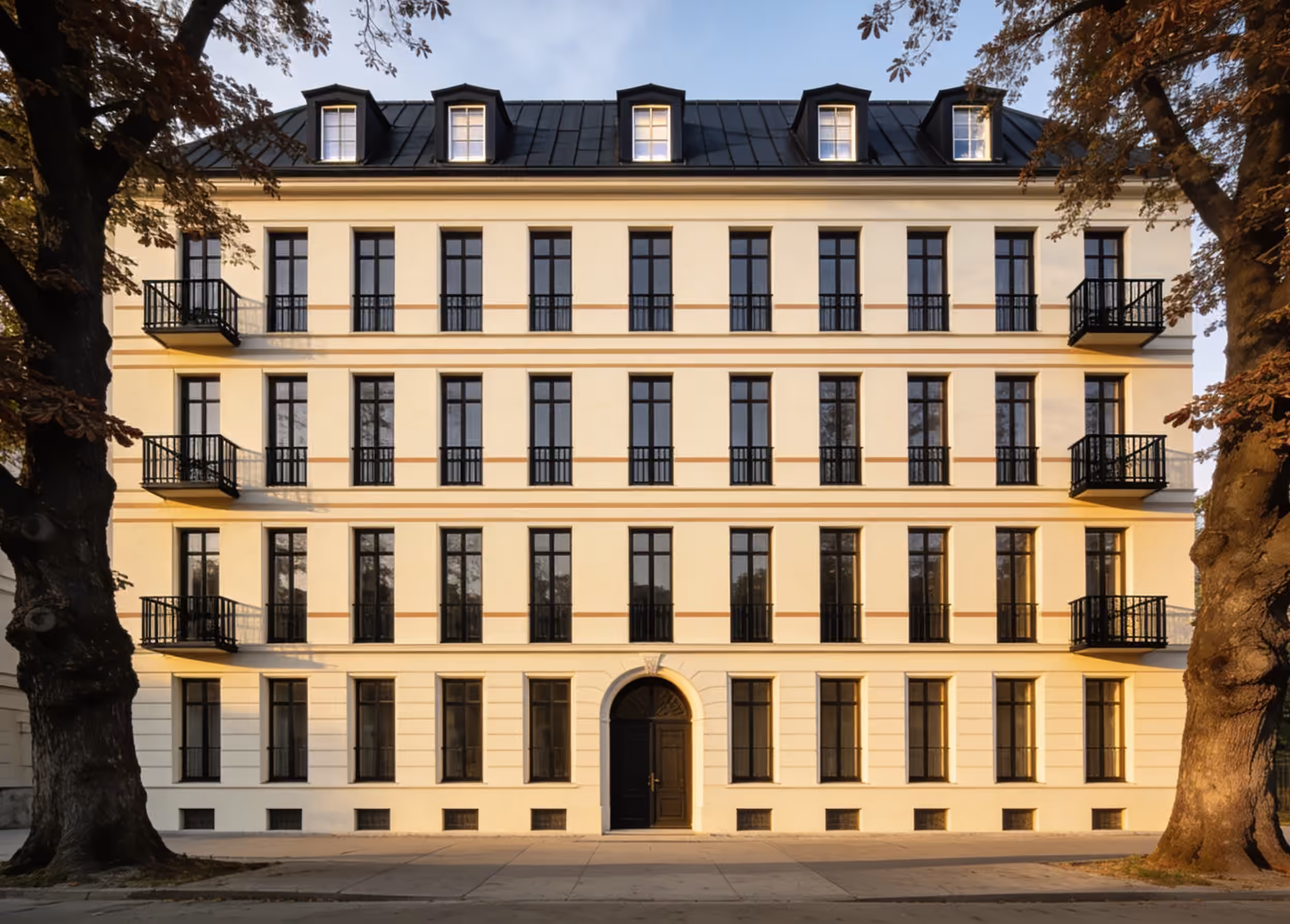 The front of Kastanienhof: a cream five-storey building with tall black windows, small iron balconies and a mansard roof with dormers, between two old chestnut trees
