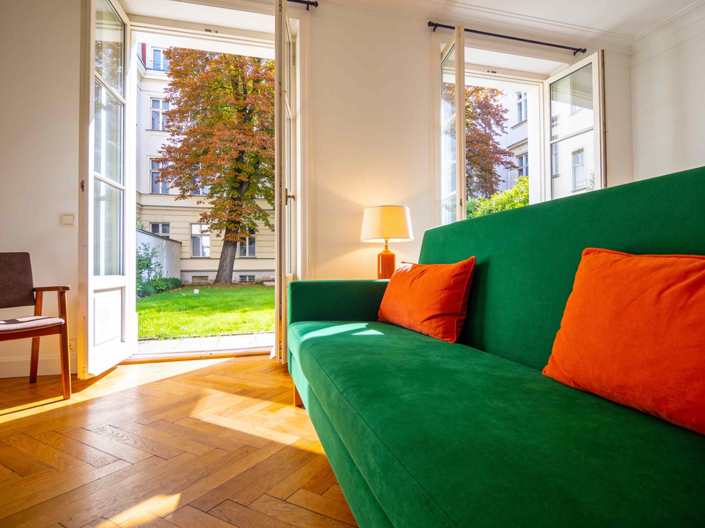 A living room with a green sofa and orange cushions, glass doors open onto a garden
