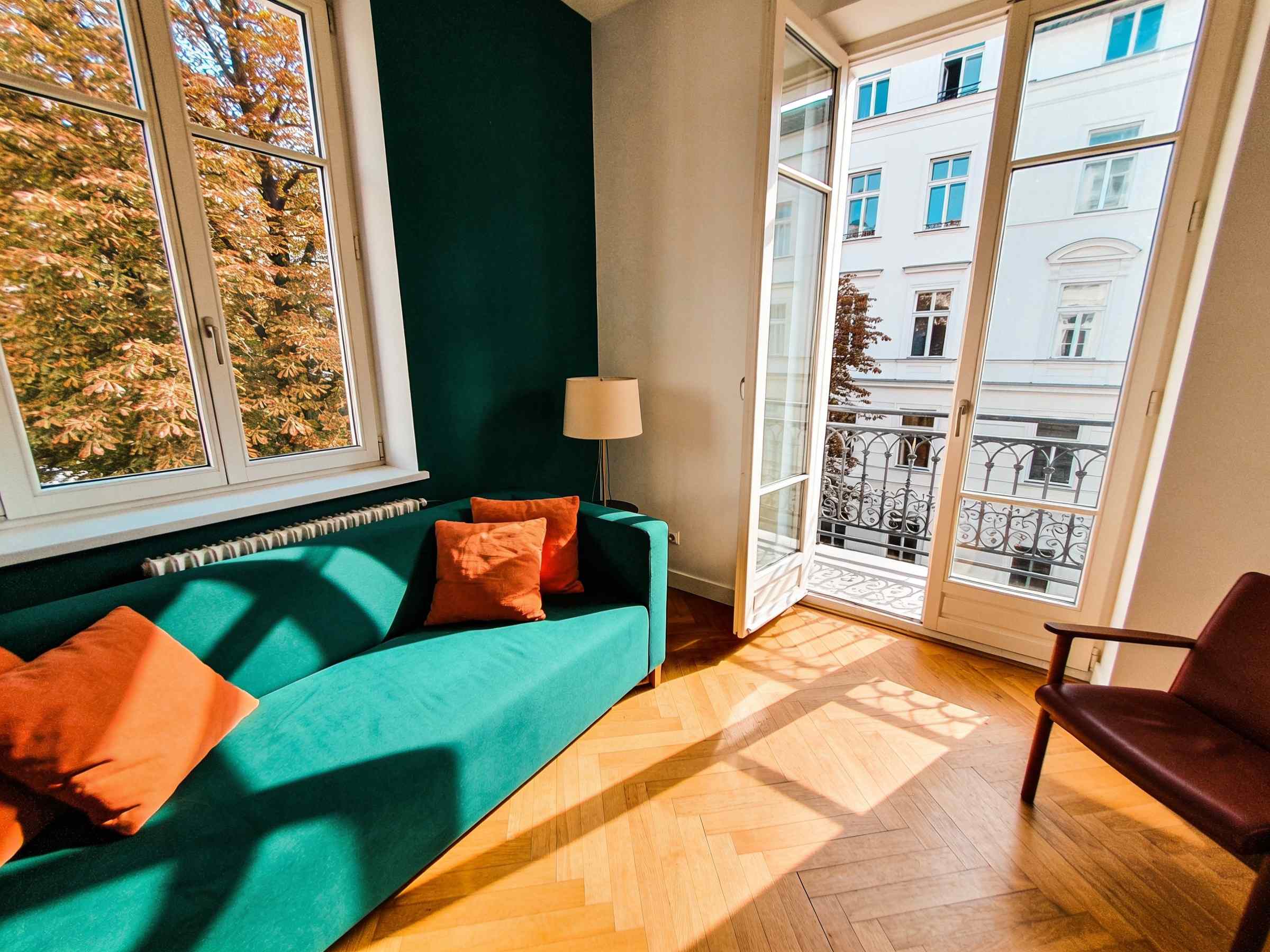 A corner living room with windows on two sides, a green sofa and parquet floor